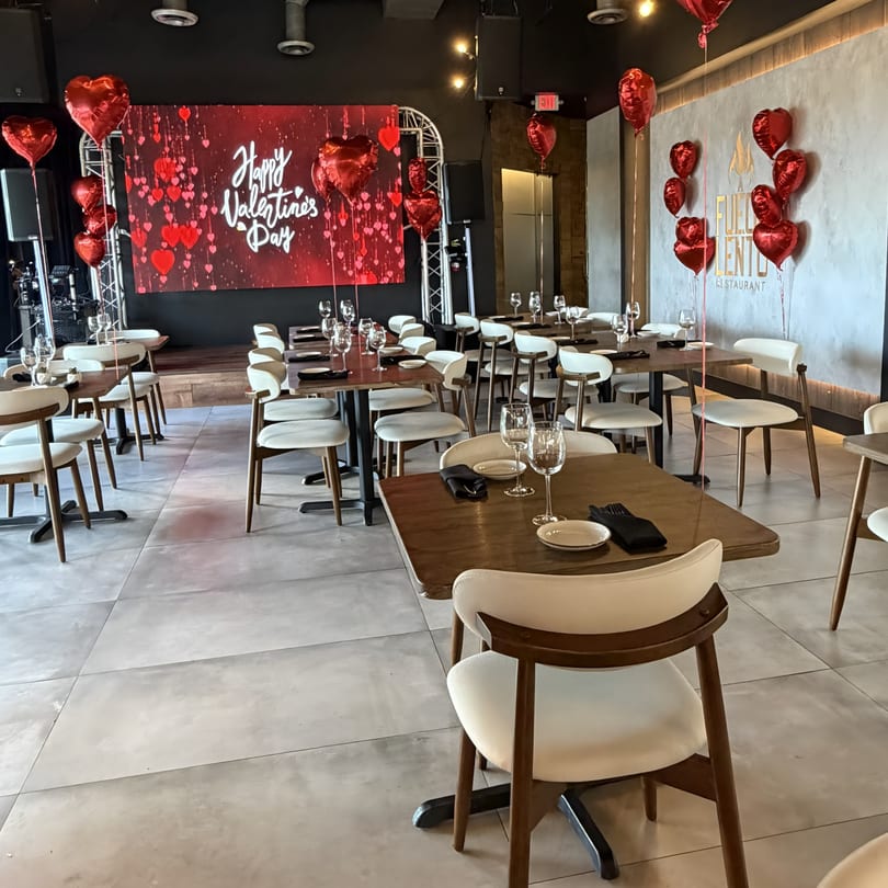A Fuego Lento Restaurant dining room decorated for Valentine's Day with red heart balloons and a large "Happy Valentine's Day" screen.