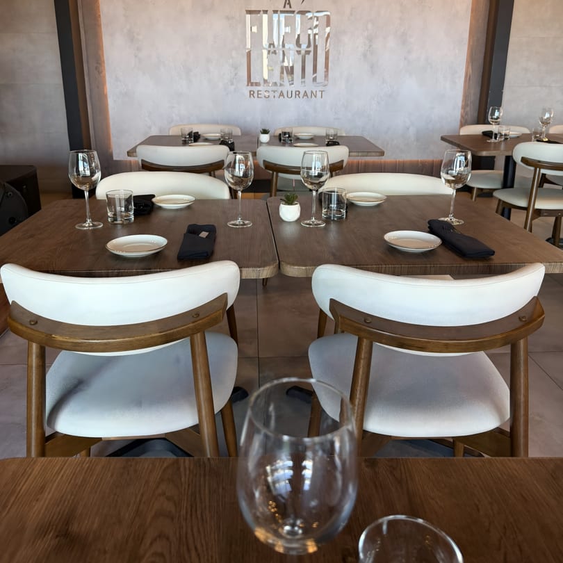 A Fuego Lento Restaurant interior with set tables, white chairs, and the restaurant logo on a concrete wall.