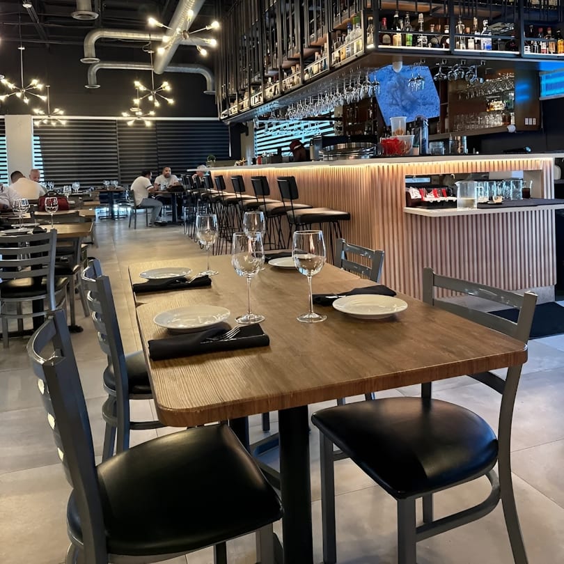 A Fuego Lento Restaurant dining room with set tables, a long bar, and patrons in the background.