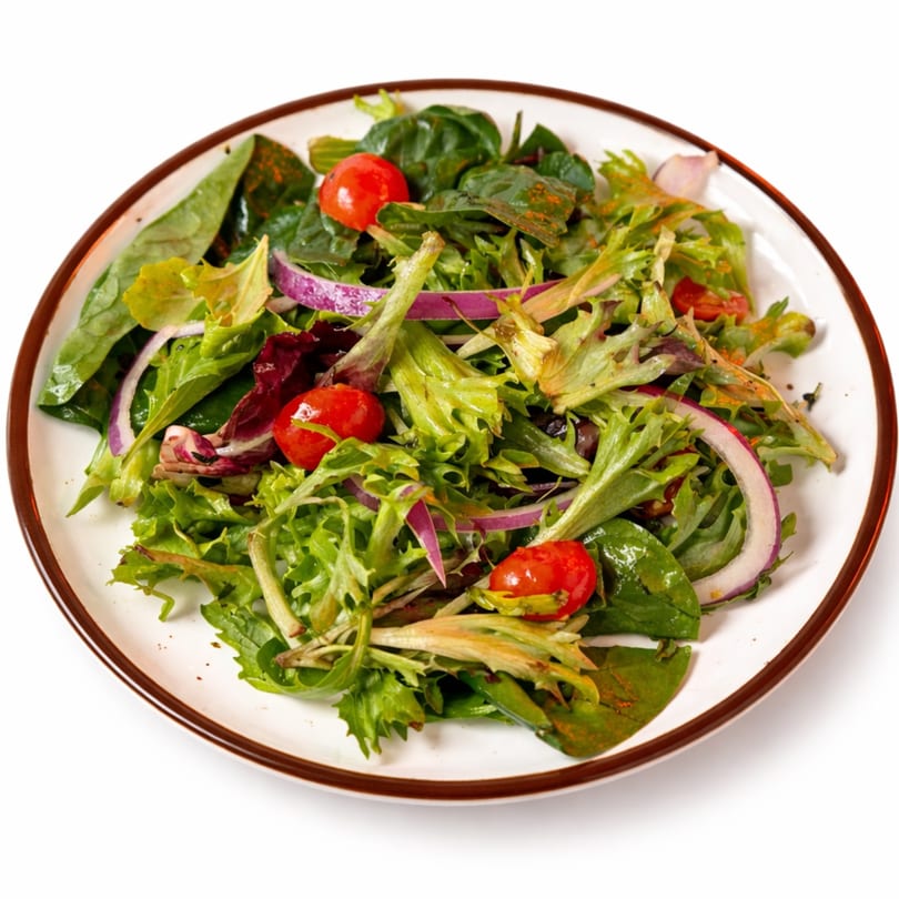 Fresh mixed green salad with cherry tomatoes and red onion on a white plate with a brown rim.