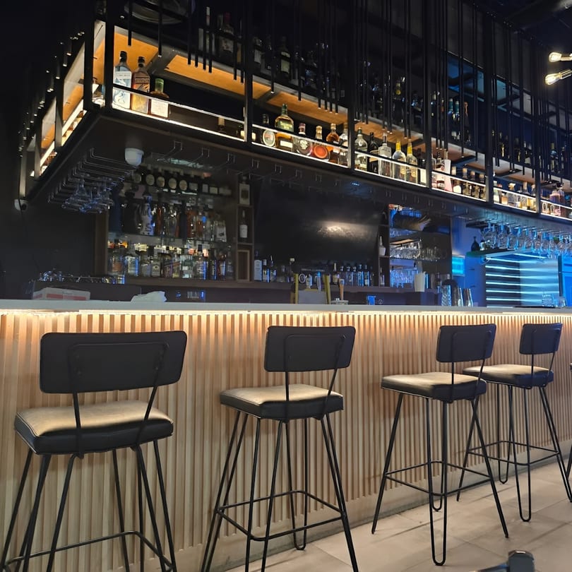 A Fuego Lento Restaurant's modern bar with liquor bottles on shelves and four bar stools.