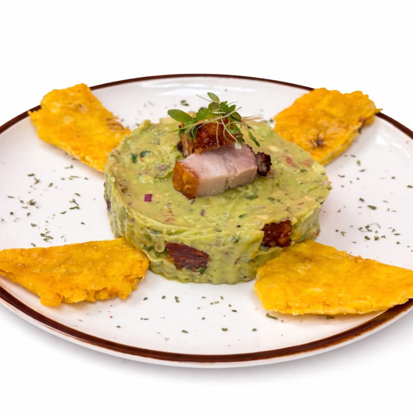 Guacamole with pork belly and plantain chips on a white plate at A Fuego Lento Restaurant.