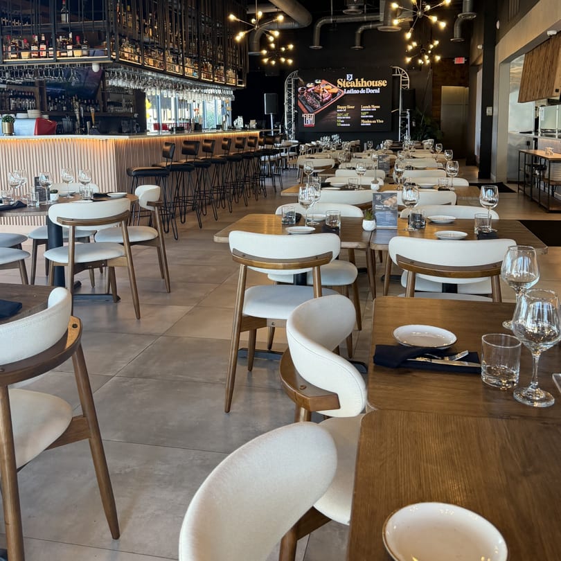 A Fuego Lento Restaurant's dining room with tables set, a bar, and a large screen displaying specials.