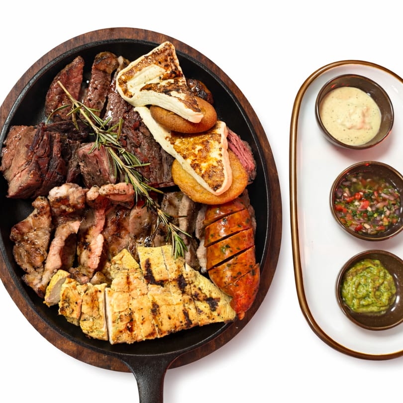 A Fuego Lento's BBQ platter with various grilled meats, cheese, and rosemary, served with three dipping sauces.